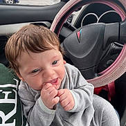 Akari joined the competition — help win amazing prizes! baby, child, car_interior, steering_wheel, pajamas, grey_clothing, hand, face, chewing, happy, person, seat, window, rain, car_mirror, storefront, pharmacy, green_shirt, pink_steering_wheel_cover, daytime