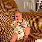 Marley is registered to the contest to win money with this photo: baby, infant, smiling, couch, indoor, onesie, clothing, happy, cute, child, person, furniture, living_room, foot, head, face, expression, relaxing, home, texture