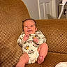 baby, infant, smiling, couch, indoor, onesie, clothing, happy, cute, child, person, furniture, living_room, foot, head, face, expression, relaxing, home, texture