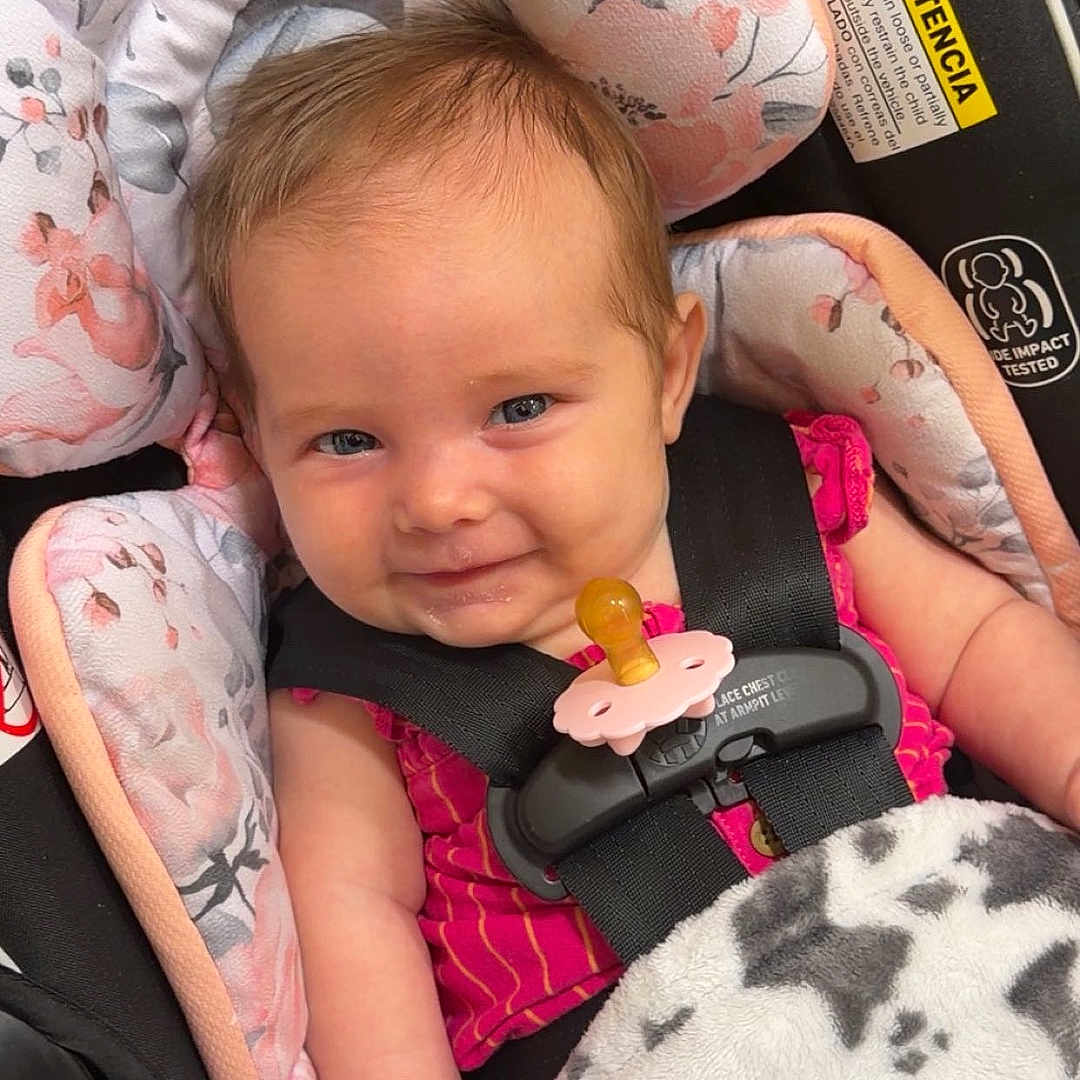 Marley joined the competition — help win amazing prizes! baby, child, car_seat, blanket, floral_pattern, smile, infant, cute, clothing, seatbelt, pink, face, head, person, safety, indoor, portrait, happy, baby_girl, cute_expression