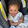 baby, child, smiling, curly_hair, blanket, car_seat, chicco, safety_warning, infant, cute, happy, seat, clothing, arm, face, portrait, indoors, baby_toddler, person, closeup