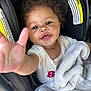 baby, child, car_seat, blanket, curly_hair, smiling, happy, reaching_hand, clothing, indoor, person, infant, cute, face, seat, soft_texture, cozy, closeup, bright_eyes, toddler