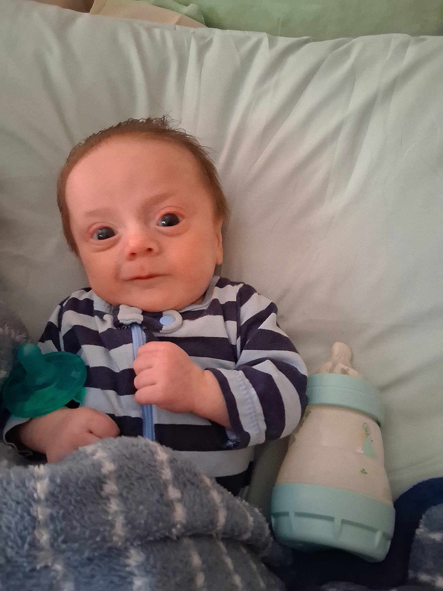 David Leo is registered to the contest to win money with this photo: baby, infant, striped_clothing, blanket, pacifier, bottle, bed, pillow, hand, face, wide_eyes, sleepwear, young_child, cute, portrait, indoors, comfort, lying_down, soft_texture, newborn