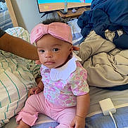 Amiylah joined the competition — help win amazing prizes! baby, bed, blankets, bow, cartoon, charging_cable, child, cute, expression, foot, furniture, hand, headband, indoor, infant, person, pink_clothing, sitting, striped_bedding, tv_screen