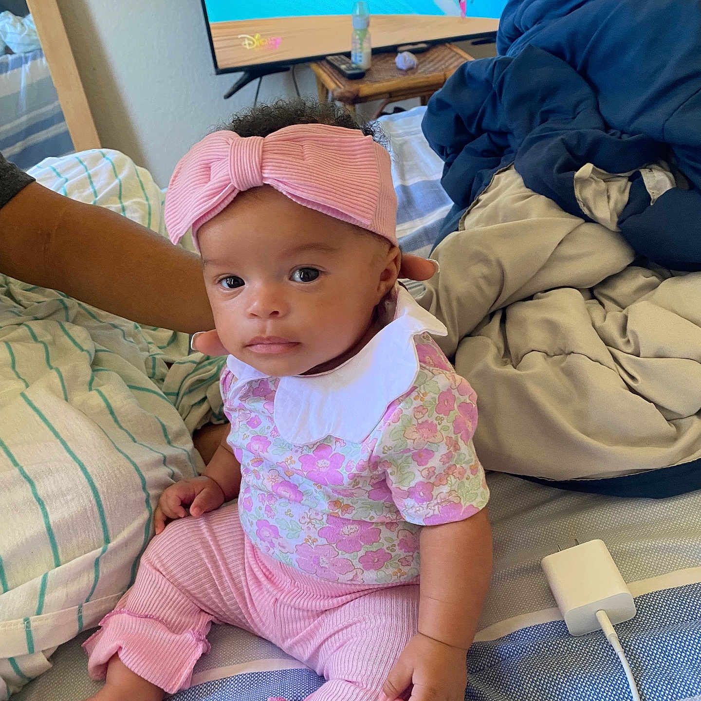 Amiylah joined the competition — help win amazing prizes! baby, bed, blankets, bow, cartoon, charging_cable, child, cute, expression, foot, furniture, hand, headband, indoor, infant, person, pink_clothing, sitting, striped_bedding, tv_screen