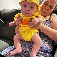 Soan participe au concours pour gagner de l'argent avec cette photo : baby, woman, couch, yellow_clothing, hat, indoor, happy, smiling, person, holding, patterned_dress, family, infant, cute, seated, home, portrait, joy, child, casual