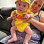 baby, woman, couch, yellow_clothing, hat, indoor, happy, smiling, person, holding, patterned_dress, family, infant, cute, seated, home, portrait, joy, child, casual