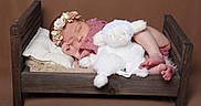 Emy participe au concours pour gagner de l'argent avec cette photo : baby, newborn, sleeping, flower_headband, wooden_bed, pillow, stuffed_animal, lamb, soft_texture, cozy, infant, portrait, cute, peaceful, pink_clothing, barefoot, indoor, brown_background, resting, child
