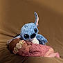 newborn, baby, sleeping, plush_toy, stitch, flower_headband, pink_lace, soft_blanket, brown_background, cute, adorable, infant, resting, toy, child, portrait, indoor, cozy, peaceful, soft_lighting
