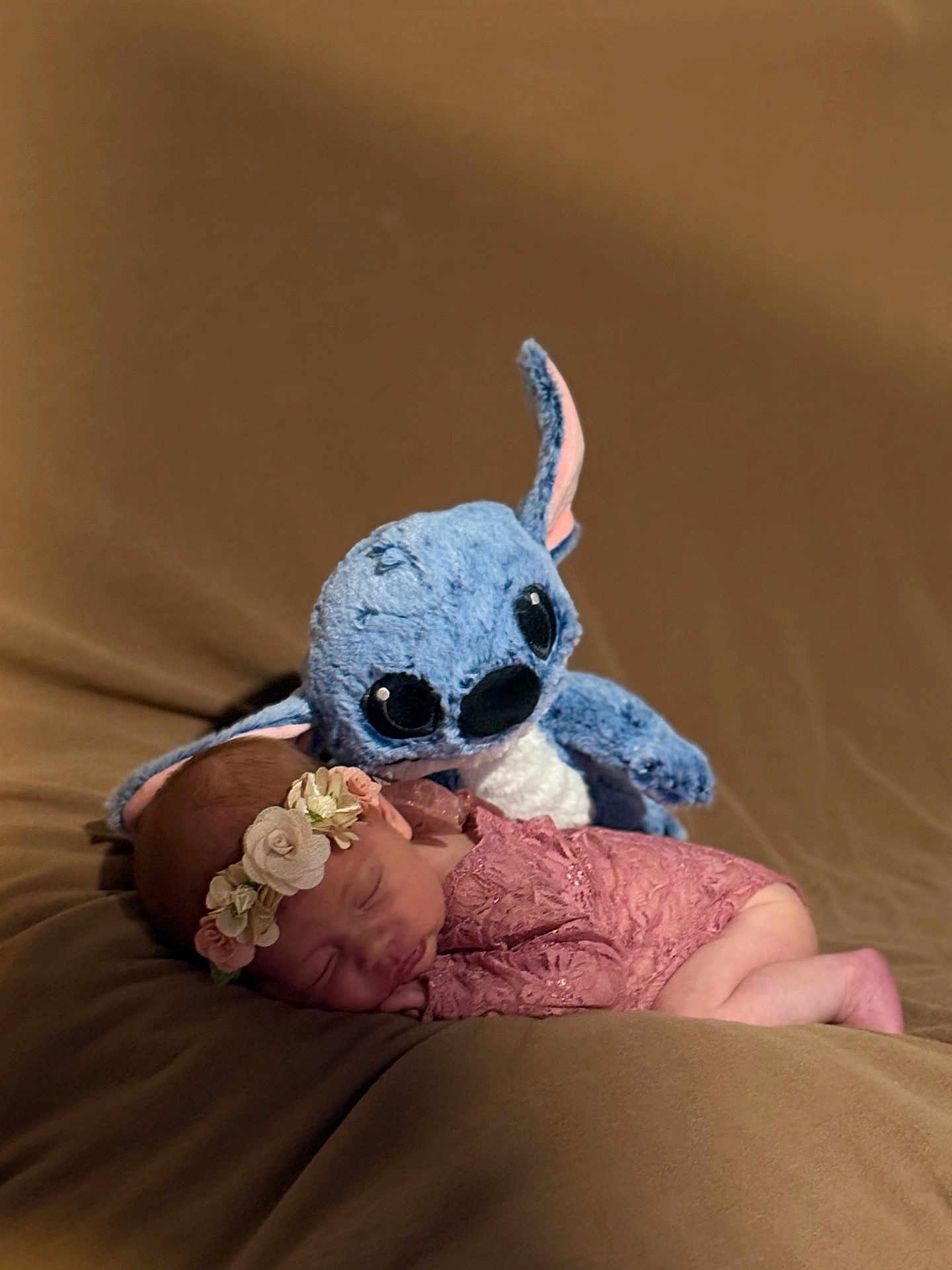 Emy a rejoint le concours — aidez-le/la à gagner de superbes lots ! newborn, baby, sleeping, plush_toy, stitch, flower_headband, pink_lace, soft_blanket, brown_background, cute, adorable, infant, resting, toy, child, portrait, indoor, cozy, peaceful, soft_lighting