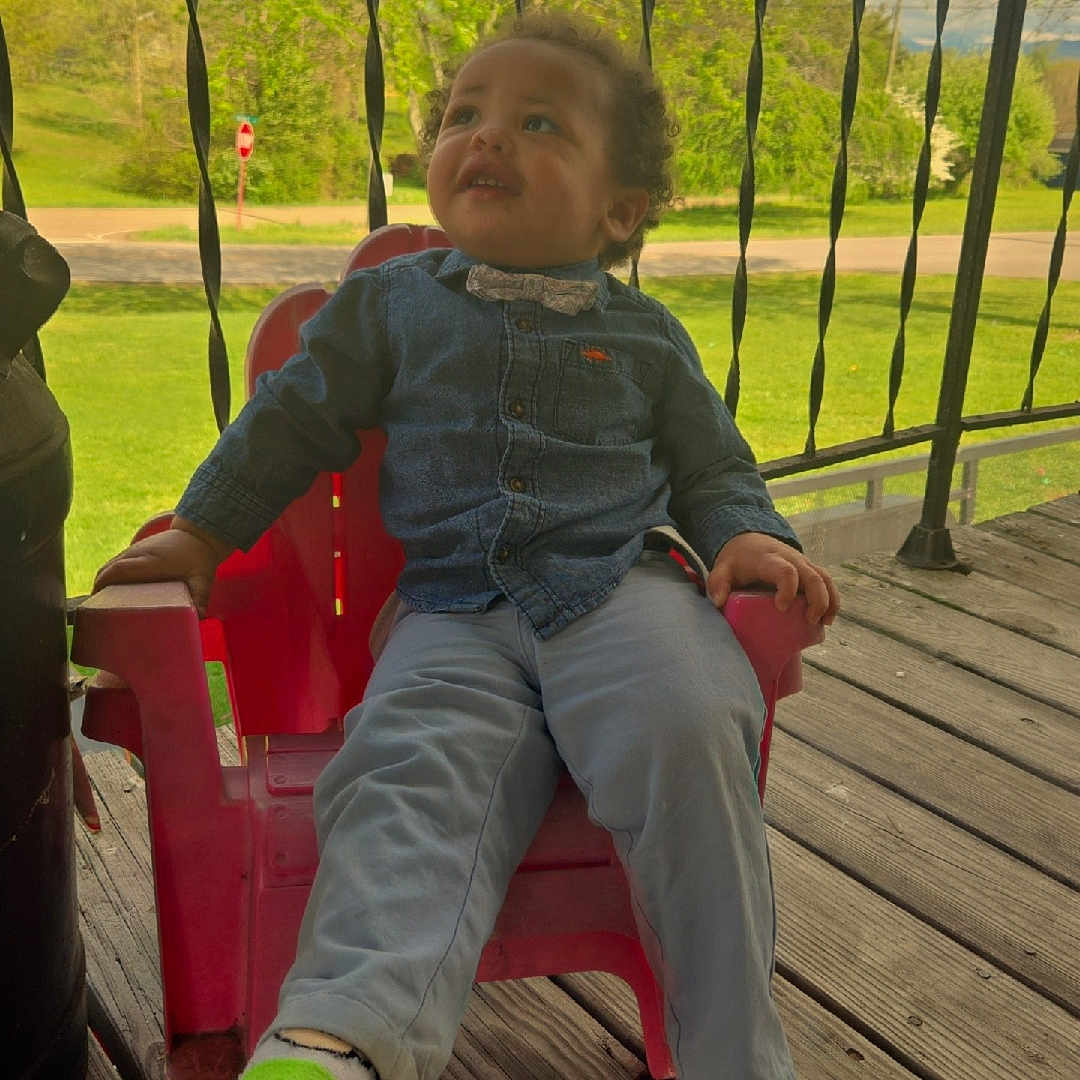 Jeremias joined the competition — help win amazing prizes! child, toddler, boy, sitting, red_chair, denim_shirt, bow_tie, gray_pants, green_socks, outdoor, deck, wooden_floor, porch, railing, spring, trees, grass, road, portrait, happy