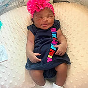 Jahmira is registered to the contest to win money with this photo: baby, child, colorful_text, comfortable, cozy, cushion, dress, flower, headband, indoor, infant, navy_blue, newborn, person, pink, resting, sleepy, smile, socks, soft_texture