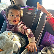 Justin is registered to the contest to win money with this photo: child, face_paint, car_seat, blanket, candy, hand, car_interior, sunlight, window, plaid_sweater, toy, purple_bag, seatbelt, smiling, curious, young, person, indoors, hair, expression