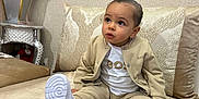Kaysan a rejoint le concours — aidez-le/la à gagner de superbes lots ! toddler, child, sitting, beige_clothing, white_shoes, couch, cushion, indoor, plant, mirror, looking_up, expression, face, young_child, fashion, home_decor, furniture, casual, portrait, cute