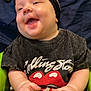 Nova is registered to the contest to win money with this photo: baby, black_clothing, blue_background, bow, casual, cheerful, child, cute, face, green_baby_seat, hands, happy, headband, indoor, infant, portrait, rolling_stones, sitting, smiling, tshirt