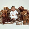 baby, smiling, basket, plush_toy, teddy_bear, brown, white_clothing, soft_texture, cozy, infant, cute, child, indoor, portrait, sitting, fabric, decorative, happy, toy, wooden_sign
