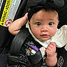 baby, infant, car_seat, black_headband, black_clothing, wide_eyes, face, hand, safety_belt, child, cute, closeup, indoors, person, expression, adorable, headwear, seatbelt, infant_girl, portrait