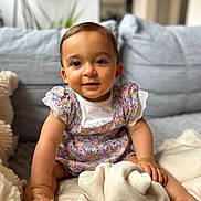 Ava a rejoint le concours — aidez-le/la à gagner de superbes lots ! baby, child, infant, sitting, couch, blanket, smiling, face, cute, indoors, soft, floral_dress, cozy, happy, person, young, skin, foot, hand, portrait