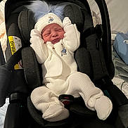 Luca is registered to the contest to win money with this photo: baby, infant, car_seat, knitwear, white_clothing, hat, mittens, pom_poms, newborn, indoor, sleepy_face, soft_texture, black_car_seat, child, cute, cozy, bundle, small_hands, sleeping, portrait