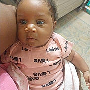 Skylar is registered to the contest to win money with this photo: baby, infant, child, pink_onesie, love_text, blanket, curly_hair, face, eyes, arm, indoor, carpet, person, human_skin, expression, holding, soft_toy, closeup, cuddly, cute