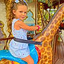 amusement_park, blue_dress, carousel, child, colorful, curly_hair, daytime, decorative, fun, giraffe, girl, hair_bow, happy, outdoor, playful, portrait, ride, seatbelt, smile, wooden_floor