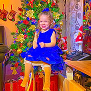 Emili participe au concours pour gagner de l'argent avec cette photo : blue_dress, carpet, child, christmas_tree, curtains, festive_lights, figurines, furniture, girl, holiday_decorations, holiday_season, indoor, joy, long_hair, presents, smiling, stockings, stool, television, white_socks