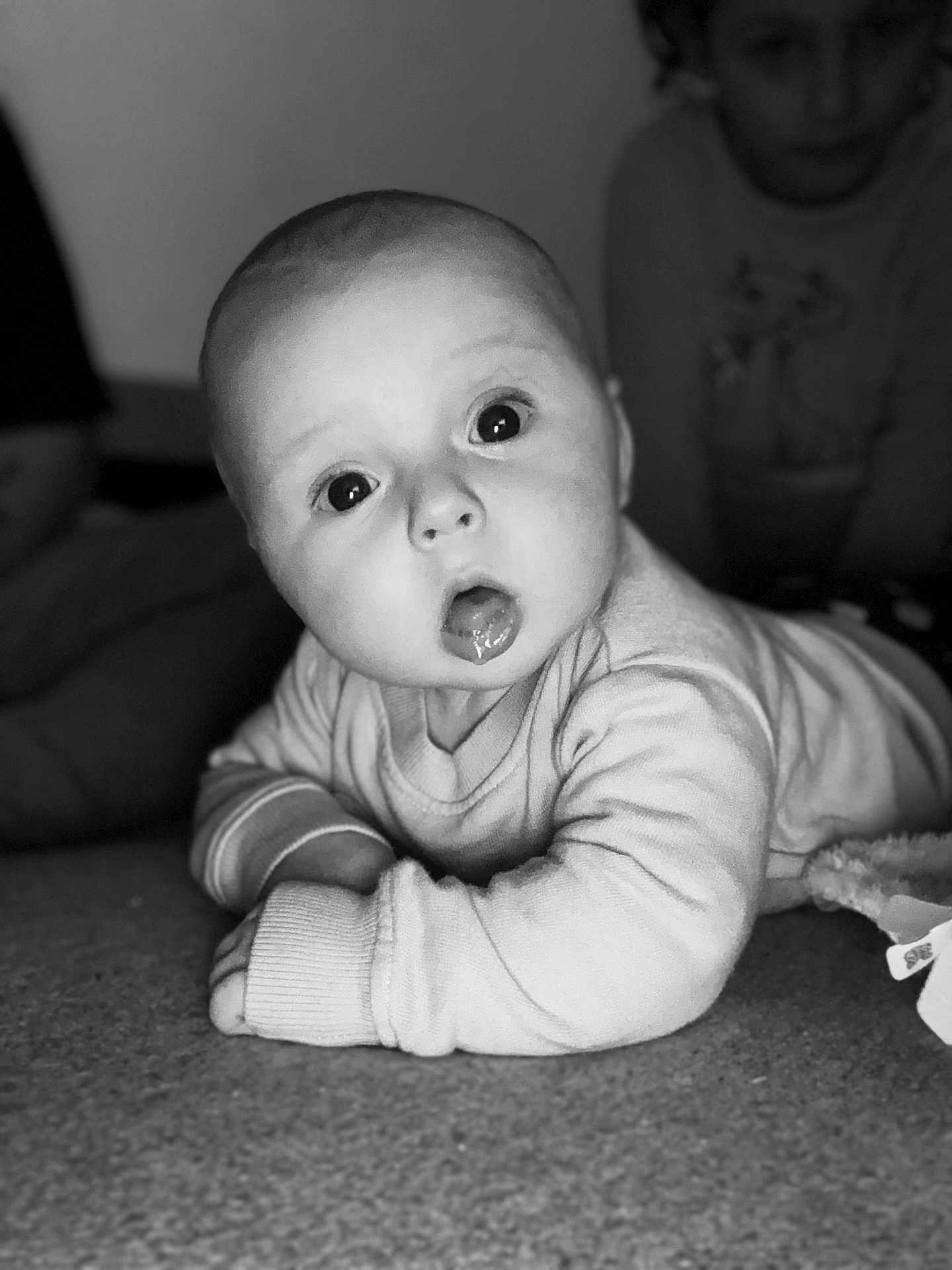 Gabriel participe au concours pour gagner de l'argent avec cette photo : baby, child, infant, black_and_white, portrait, curious, tummy_time, indoors, wide_eyes, sweater, carpet, person, expression, candid, family, soft_light, young_child, face, background, observer