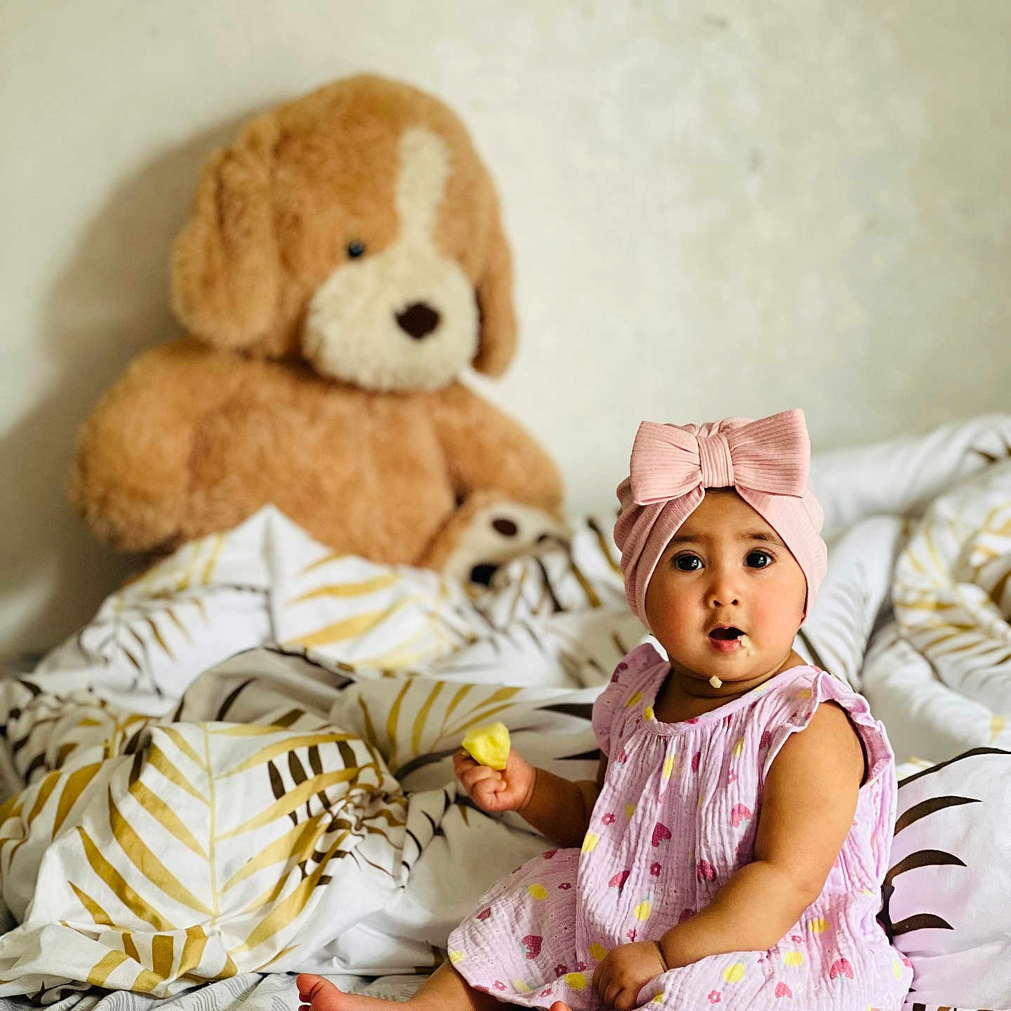 Aliza a rejoint le concours — aidez-le/la à gagner de superbes lots ! baby, bed, blanket, bow, child, cozy, cute, face, furniture, headband, indoor, infant, patterned_sheet, pink_dress, portrait, sitting, snack, soft_toy, teddy_bear, toy