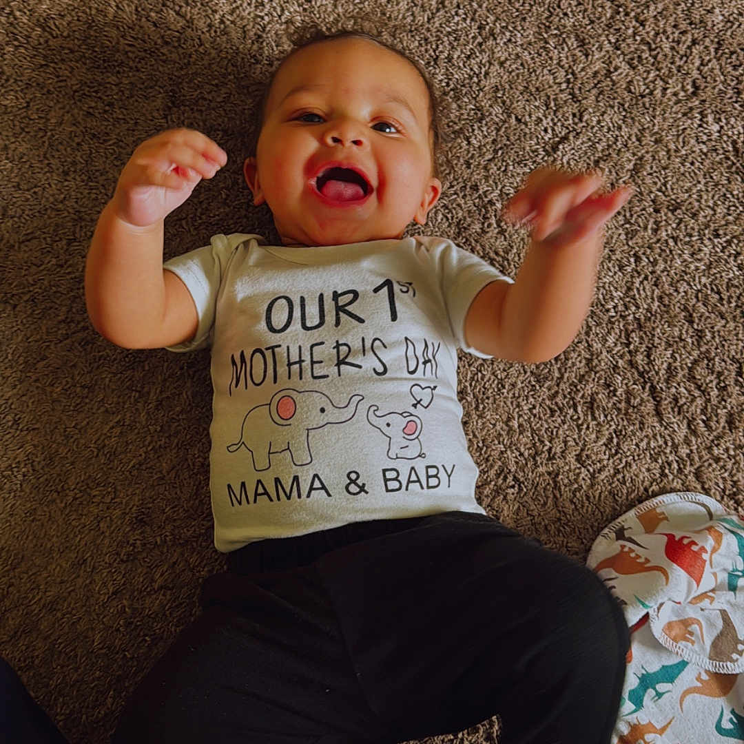 Kaiden joined the competition — help win amazing prizes! baby, child, smiling, carpet, clothing, tshirt, happy, indoor, infant, lying_down, person, blanket, animal_print, floor, cute, celebration, mother's_day, raised_hands, cheerful, casual