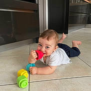 Oscar a rejoint le concours — aidez-le/la à gagner de superbes lots ! baby, child, toy, floor, kitchen, tile_floor, cabinets, door, smiling, playing, colorful, stacking_cups, indoor, person, infant, casual_clothing, happy, cute, home, crawling