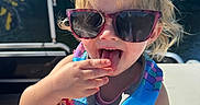 Everleigh is registered to the contest to win money with this photo: blue_sky, boat, child, colorful, girl, hand, life_jacket, open_mouth, outdoor, playful, portrait, seated, smiling, summer, sunglasses, sunlight, swimwear, toddler, tongue, trees