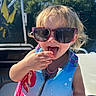 Everleigh is registered to the contest to win money with this photo: child, toddler, girl, sunglasses, smiling, open_mouth, tongue, hand, life_jacket, swimwear, colorful, outdoor, sunlight, blue_sky, trees, boat, seated, portrait, summer, playful