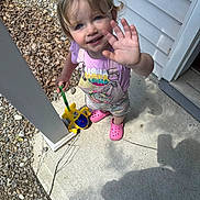 Everleigh joined the competition — help win amazing prizes! child, toddler, smiling, waving, outdoor, porch, driveway, house, concrete, gravel, toy, toy_vehicle, pink_clogs, overalls, purple_shirt, blonde_hair, blue_eyes, portrait, daylight, happy