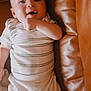 baby, infant, smiling, face, person, striped_shirt, white_pants, couch, leather, cozy, indoors, cute, happy, child, young, lying_down, hand, expression, comfort, soft_lighting