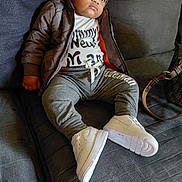Brayden Cherry is registered to the contest to win money with this photo: child, kid, beanie, hat, jacket, white_sneakers, pants, couch, sofa, bag, fashion, indoor, portrait, clothing, casual, footwear, person, sitting, young, expression