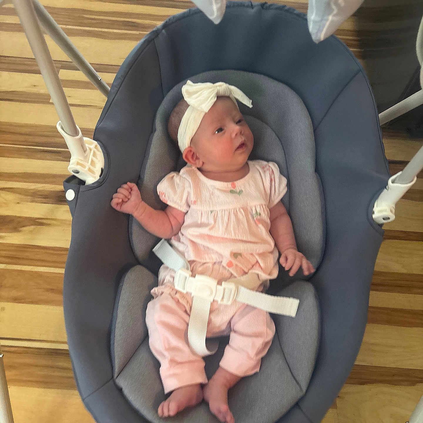 Jasmine is registered to the contest to win money with this photo: baby, infant, baby_swing, headband, pink_clothing, wooden_floor, indoor, child, newborn, cute, comfort, relaxing, buckle, seat, safety_strap, small_hands, small_feet, portrait, resting, adorable