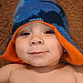 baby, child, hat, knit_hat, blue, orange, smile, face, skin, person, lying_down, carpet, cheeky, cute, headwear, indoors, infant, happy, closeup, portrait