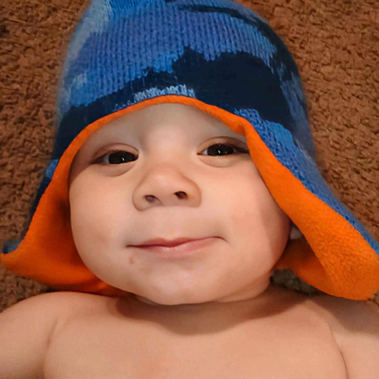 Zy'Ael is registered to the contest to win money with this photo: baby, blue, carpet, cheeky, child, closeup, cute, face, happy, hat, headwear, indoors, infant, knit_hat, lying_down, orange, person, portrait, skin, smile