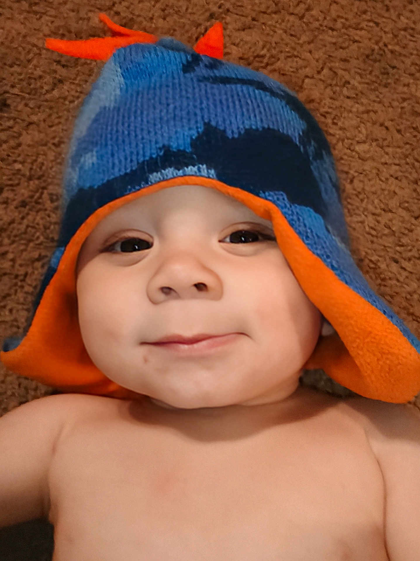 Zy'Ael is registered to the contest to win money with this photo: baby, child, hat, knit_hat, blue, orange, smile, face, skin, person, lying_down, carpet, cheeky, cute, headwear, indoors, infant, happy, closeup, portrait
