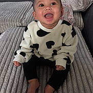 Zariya is registered to the contest to win money with this photo: baby, bare_feet, bed, black_pants, blanket, child, cow_print, cozy, eyes, face, happy, indoor, infant, open_mouth, photography, pillows, portrait, sitting, smiling, sweater