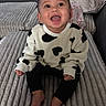 baby, bare_feet, bed, black_pants, blanket, child, cow_print, cozy, eyes, face, happy, indoor, infant, open_mouth, photography, pillows, portrait, sitting, smiling, sweater