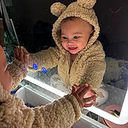 Zariya is registered to the contest to win money with this photo: baby, child, infant, mirror, reflection, smiling, happy, teddy_bear_hood, fleece_outfit, hooded_jacket, bathroom, countertop, sink, toiletries, indoor, portrait, close_up, hand, parent, playful