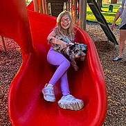 Whiskeydawn is registered to the contest to win money with this photo: child, dog, slide, playground, outdoor, glasses, happy, smiling, park, daylight, casual_clothing, purple_pants, sneakers, wood_chips, play_equipment, tree, person, pet, fun, leisure