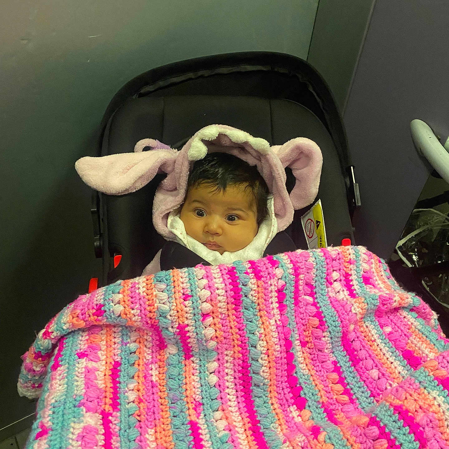 Noumidia a rejoint le concours — aidez-le/la à gagner de superbes lots ! baby, blanket, blue, bunny_ears, car_seat, child, clothing, colorful, crocheted_blanket, cute, expression, face, hoodie, indoor, orange, person, pink, purple, seated, warm