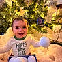 Jordan joined the competition — help win amazing prizes! baby, child, smiling, christmas_tree, ornaments, holiday, decorations, snowballs, box, blanket, cozy, indoor, festive, warm_lighting, cute, happy, person, sitting, clothing, face
