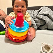 Axson joined the competition — help win amazing prizes! baby, child, smiling, toy, colorful, stackable_toy, pacifier, bed, blanket, curly_hair, happy, indoors, person, infant, playful, tattoo, hand, foot, face, expression