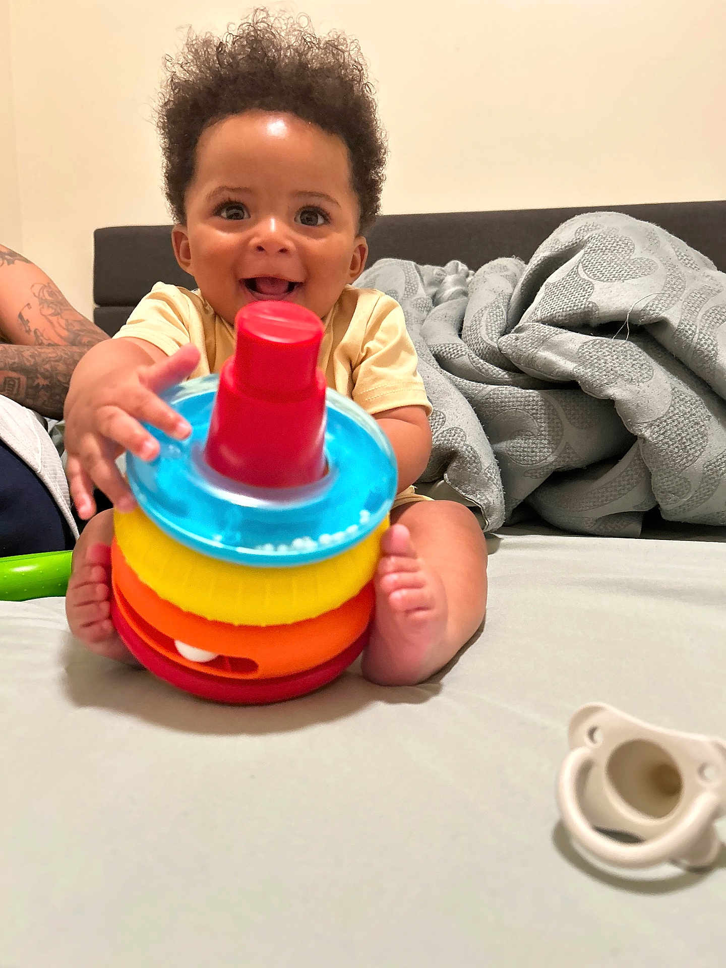 Axson joined the competition — help win amazing prizes! baby, child, smiling, toy, colorful, stackable_toy, pacifier, bed, blanket, curly_hair, happy, indoors, person, infant, playful, tattoo, hand, foot, face, expression