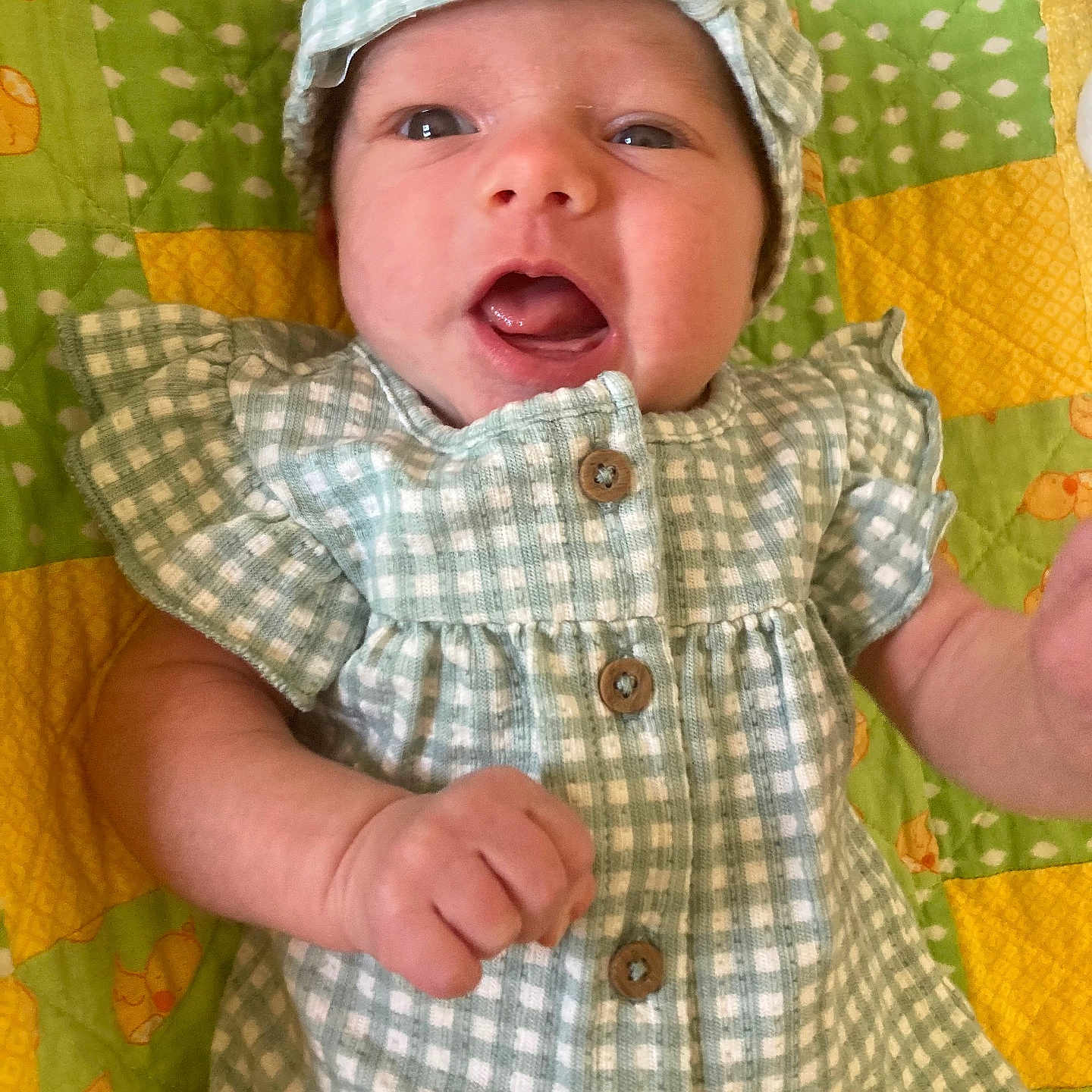 Raegan is registered to the contest to win money with this photo: arm, baby, blanket, buttons, cute, dress, eyes, face, gingham, green, hand, headband, infant, lying_down, newborn, open_mouth, portrait, quilt, smiling, yellow