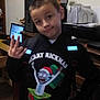 child, boy, hoodie, christmas, cartoon, indoor, pose, desk, computer, office_supplies, furniture, tile_floor, hand_gesture, smile, casual, young, clothing, person, room, celebration