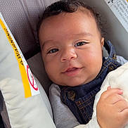 Isaac is registered to the contest to win money with this photo: baby, child, face, smile, car_seat, blanket, clothing, denim, button, hand, skin, eyelashes, curly_hair, portrait, infant, indoor, cute, comfort, seat, soft
